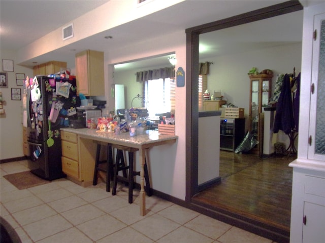 kitchen with light wood-type flooring, black fridge, and light brown cabinetry