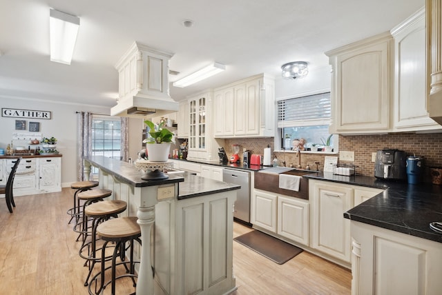 kitchen featuring decorative backsplash, sink, stainless steel dishwasher, light hardwood / wood-style flooring, and a center island