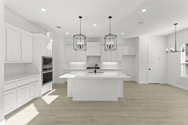 kitchen with appliances with stainless steel finishes, light hardwood / wood-style flooring, a kitchen island with sink, and white cabinets