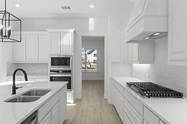 kitchen featuring appliances with stainless steel finishes, sink, white cabinetry, light hardwood / wood-style flooring, and premium range hood