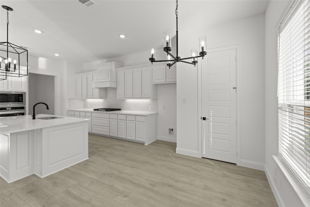 kitchen with appliances with stainless steel finishes, sink, light wood-type flooring, hanging light fixtures, and white cabinetry