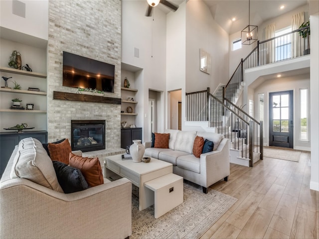 living room with built in shelves, a fireplace, a high ceiling, light hardwood / wood-style floors, and a notable chandelier