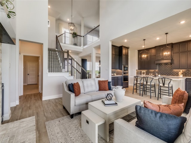 living room with sink, a towering ceiling, light hardwood / wood-style flooring, and an inviting chandelier