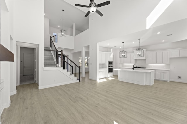 unfurnished living room featuring sink, light hardwood / wood-style flooring, a high ceiling, and ceiling fan with notable chandelier