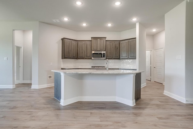 kitchen featuring light stone countertops, a center island with sink, and light hardwood / wood-style floors