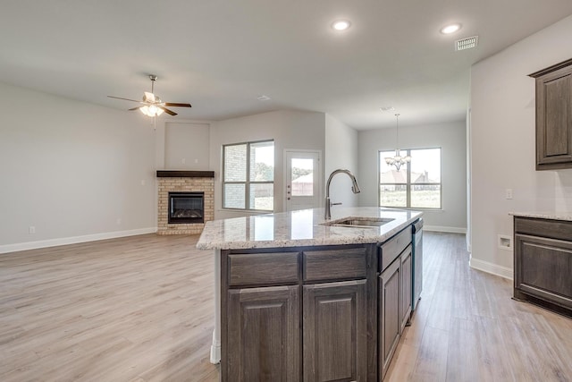 kitchen featuring sink, dishwasher, a kitchen island with sink, hanging light fixtures, and a brick fireplace