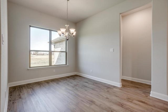 empty room featuring a notable chandelier and light wood-type flooring