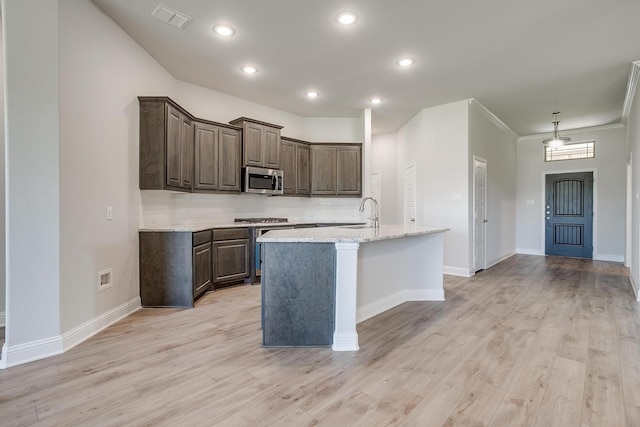 kitchen with light stone counters, ornamental molding, stainless steel appliances, a center island with sink, and light hardwood / wood-style floors