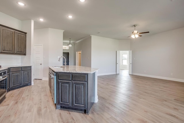 kitchen with a kitchen island with sink, sink, dark brown cabinets, and light wood-type flooring