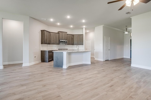 kitchen with backsplash, ceiling fan, a center island with sink, and light hardwood / wood-style floors