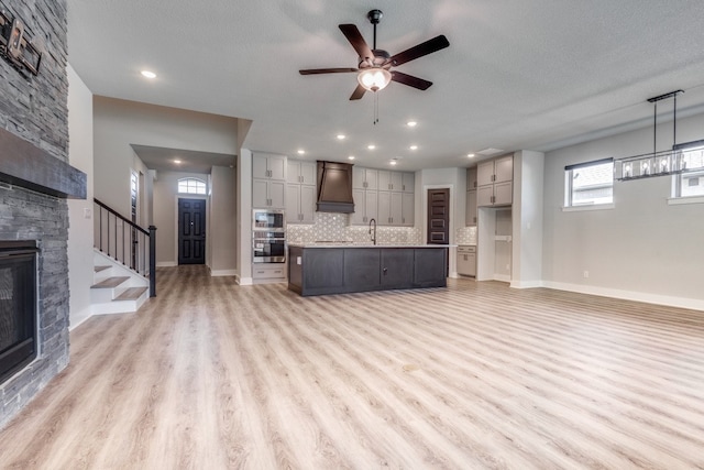 unfurnished living room featuring a stone fireplace, sink, light wood-type flooring, a textured ceiling, and ceiling fan