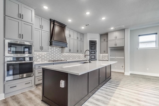 kitchen with decorative backsplash, an island with sink, sink, gray cabinets, and appliances with stainless steel finishes