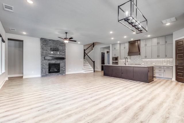 kitchen featuring decorative backsplash, custom range hood, gray cabinetry, a center island with sink, and light hardwood / wood-style floors