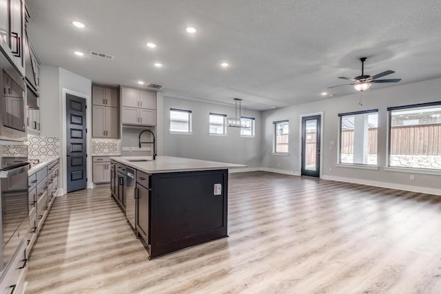 kitchen featuring a kitchen island with sink, backsplash, sink, decorative light fixtures, and light wood-type flooring