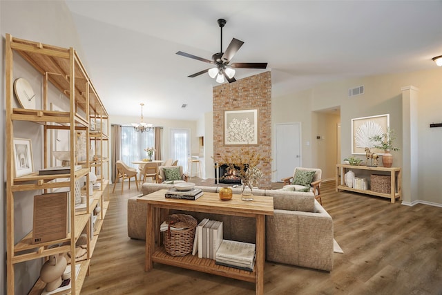 living room with a fireplace, ceiling fan with notable chandelier, dark wood-type flooring, and vaulted ceiling