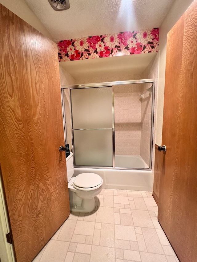 bathroom with a textured ceiling, shower / bath combination with glass door, and toilet