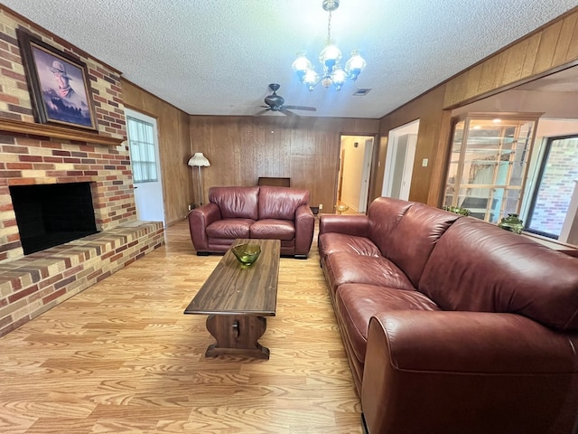 living room featuring a textured ceiling, ceiling fan with notable chandelier, a fireplace, and light hardwood / wood-style flooring