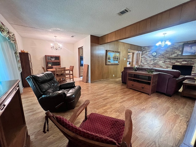 living room featuring light hardwood / wood-style flooring, a chandelier, a textured ceiling, and wood walls