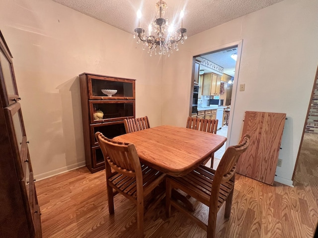 dining room featuring a textured ceiling, light hardwood / wood-style floors, and an inviting chandelier