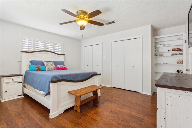 bedroom with ceiling fan, dark hardwood / wood-style flooring, multiple closets, and a textured ceiling