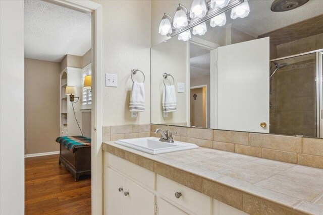 bathroom featuring a textured ceiling, hardwood / wood-style flooring, vanity, decorative backsplash, and tiled shower