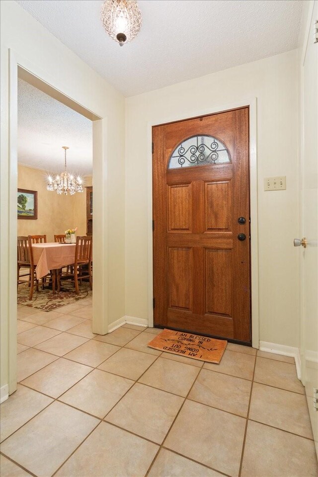 foyer entrance featuring light tile patterned floors, a textured ceiling, and an inviting chandelier