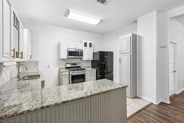 kitchen featuring stainless steel appliances, light stone countertops, sink, white cabinetry, and hardwood / wood-style flooring