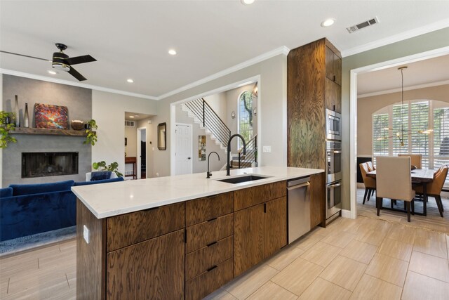 kitchen featuring a large fireplace, stainless steel appliances, sink, ceiling fan, and ornamental molding