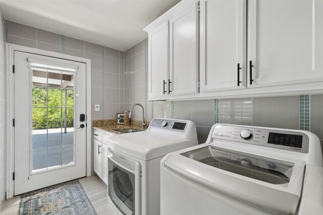 clothes washing area featuring cabinets, separate washer and dryer, light hardwood / wood-style flooring, sink, and tile walls