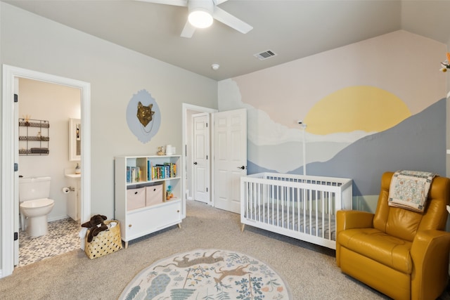 bedroom featuring a crib, ensuite bathroom, ceiling fan, and carpet floors