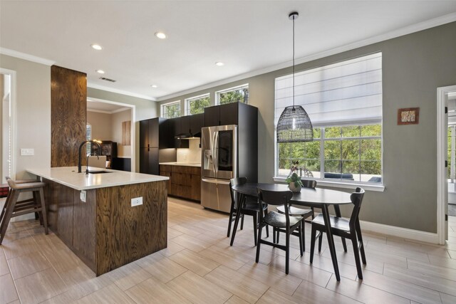 kitchen featuring pendant lighting, stainless steel fridge with ice dispenser, kitchen peninsula, ornamental molding, and sink