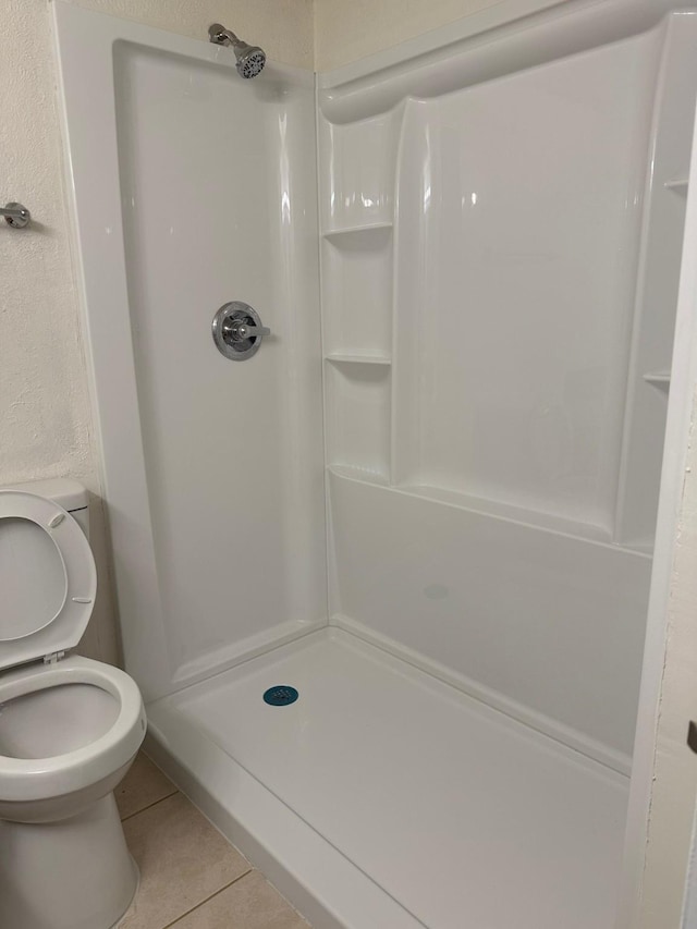 bathroom featuring a stall shower, toilet, and tile patterned floors