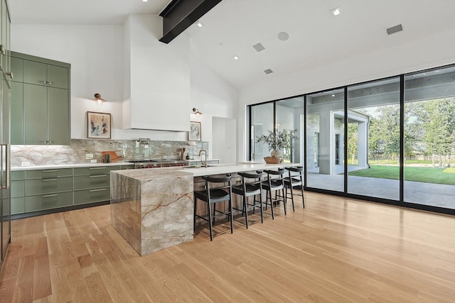 kitchen with decorative backsplash, a breakfast bar, green cabinets, and high vaulted ceiling