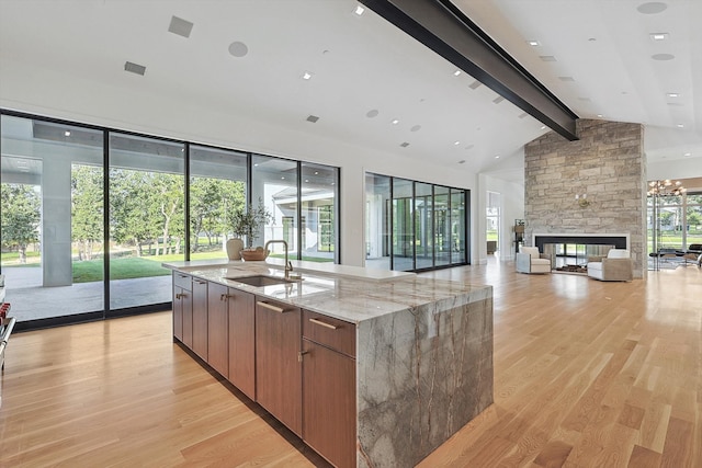 kitchen with light stone countertops, beamed ceiling, a fireplace, light hardwood / wood-style floors, and sink