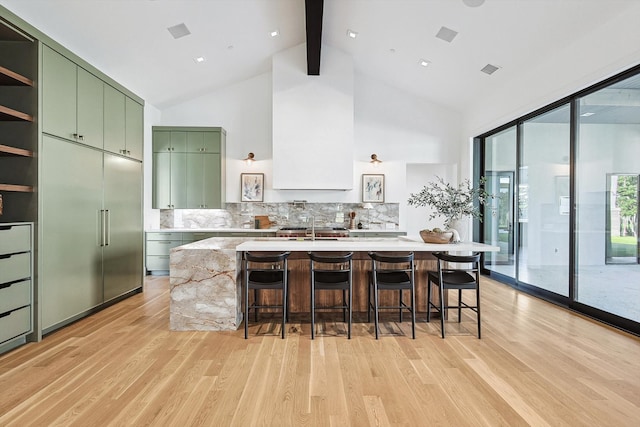 kitchen featuring tasteful backsplash, green cabinets, light wood-type flooring, a breakfast bar area, and built in fridge