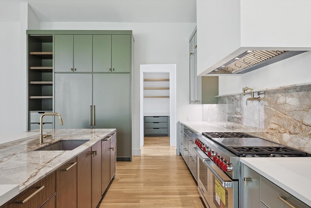 kitchen with green cabinets, custom range hood, range with two ovens, light stone countertops, and sink