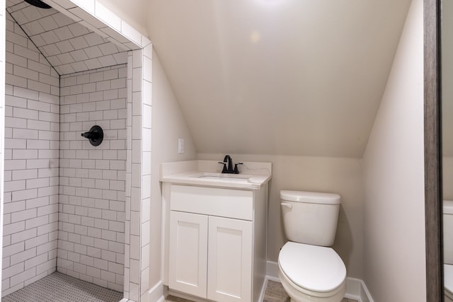 bathroom with a tile shower, vanity, vaulted ceiling, and toilet