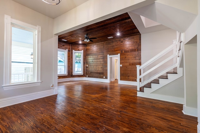 unfurnished living room with ceiling fan, wood-type flooring, and wooden walls