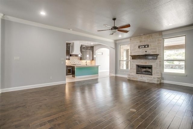 unfurnished living room with dark wood-type flooring, a fireplace, a textured ceiling, and ornamental molding