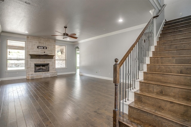 unfurnished living room with crown molding, a textured ceiling, a stone fireplace, dark hardwood / wood-style floors, and ceiling fan