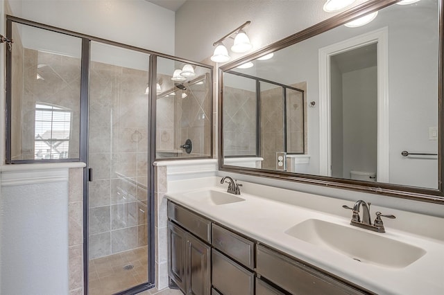 bathroom featuring a shower with door, double sink vanity, and toilet