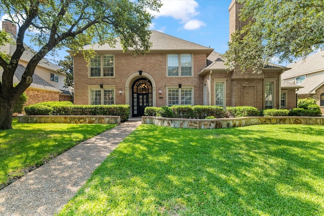 view of front of home with a front yard, french doors, brick siding, and roof with shingles