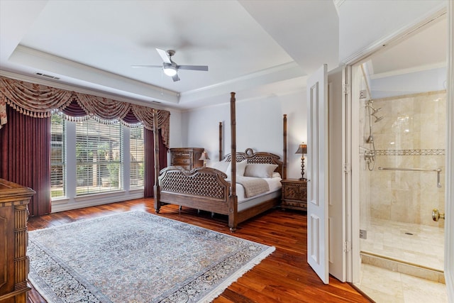 bedroom featuring dark wood finished floors, a raised ceiling, visible vents, ornamental molding, and ensuite bath