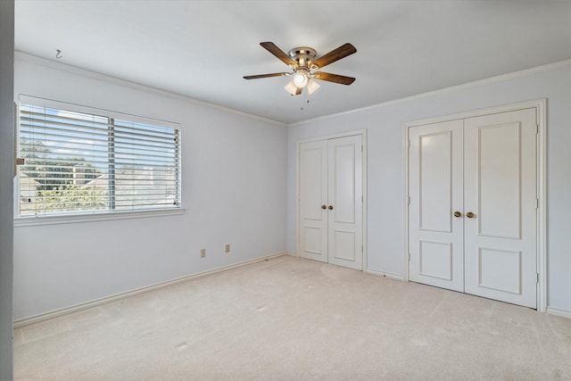 unfurnished bedroom featuring multiple closets, light colored carpet, crown molding, and ceiling fan