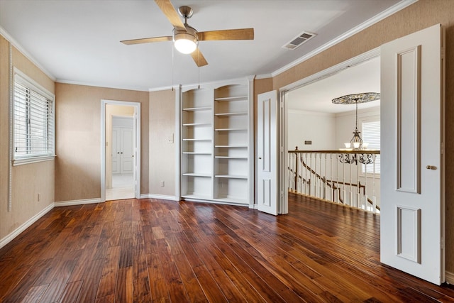 spare room featuring built in shelves, dark wood finished floors, visible vents, ornamental molding, and baseboards