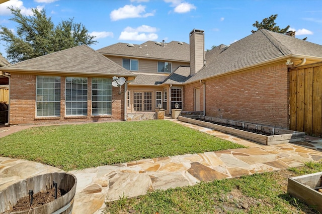 back of property with a shingled roof, a garden, fence, a yard, and brick siding