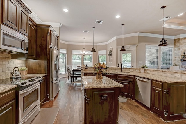 kitchen featuring appliances with stainless steel finishes, sink, decorative light fixtures, light wood-type flooring, and a kitchen island