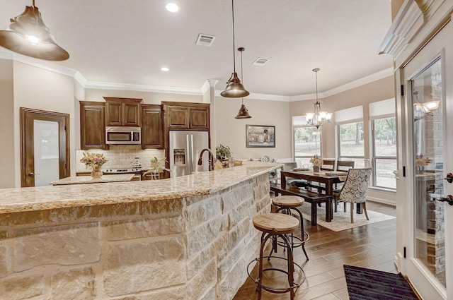 kitchen with decorative backsplash, appliances with stainless steel finishes, light stone counters, ornamental molding, and dark hardwood / wood-style floors