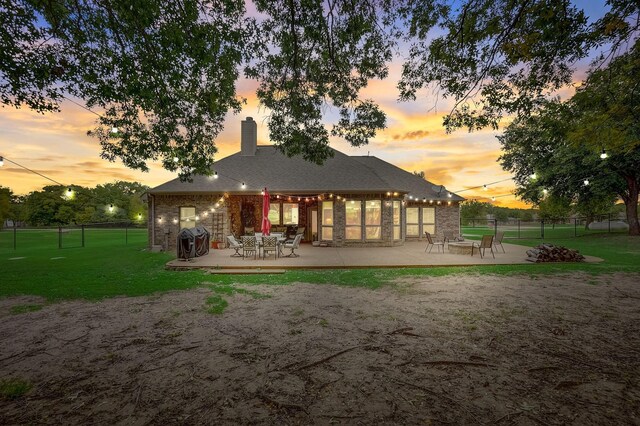 back house at dusk featuring a patio and a yard