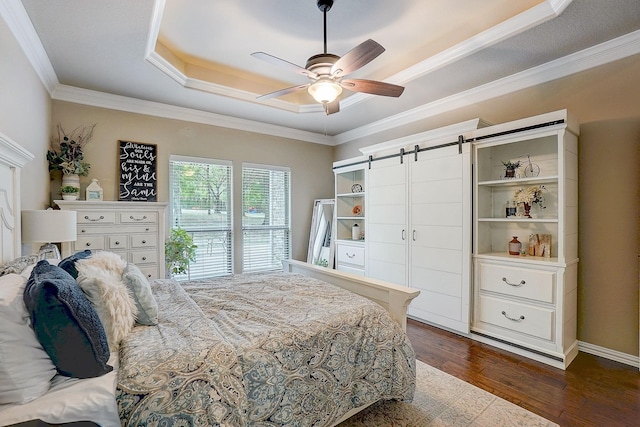 bedroom with dark hardwood / wood-style flooring, ornamental molding, a tray ceiling, ceiling fan, and a barn door